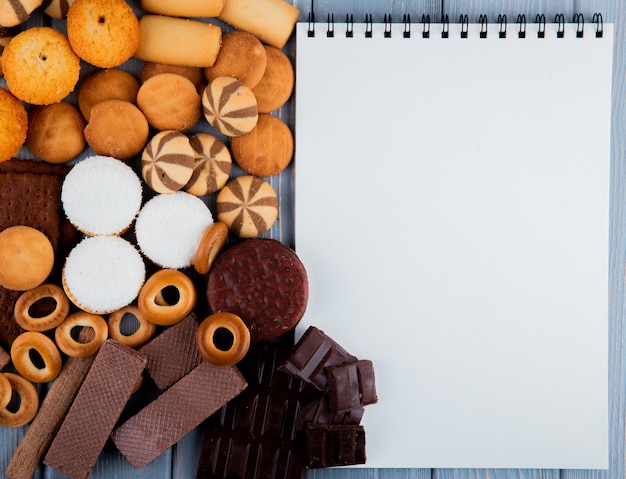 Foto gratuita vista dall'alto copia spazio mix di biscotti con cialde al cioccolato e un quaderno bianco