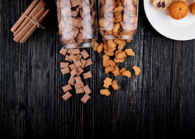 Top view copy space cookies in a jar of cornflakes and corn sticks on a black wooden background