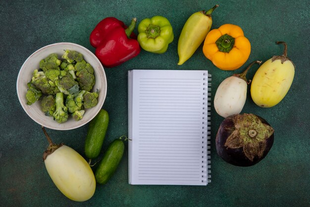 Top view  copy space copybook with cucumbers and bell peppers and broccoli on green background