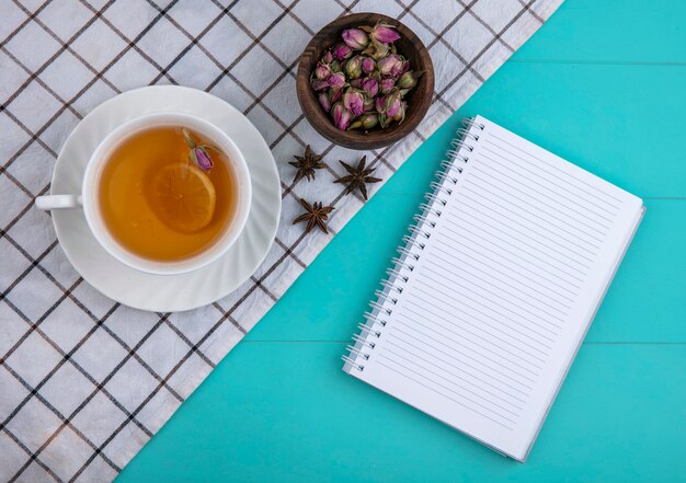 Top view copy space cup of tea with a slice of lemon and a notebook with dried flowers on a light blue background