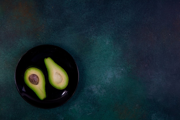 Free photo top view copy space cut in half avocado on a black plate on a dark green background