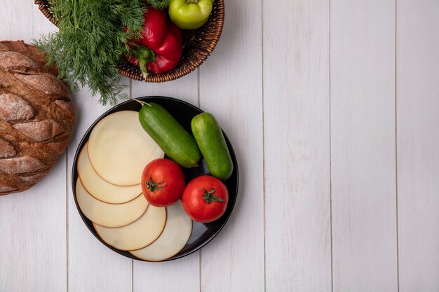 Top view  copy space dill with bell peppers in a basket with smoked cheese  tomatoes and cucumbers  on white background