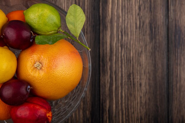 Top view  copy space fruit mix lemons  limes  plums  peaches and oranges in a vase on a wooden background