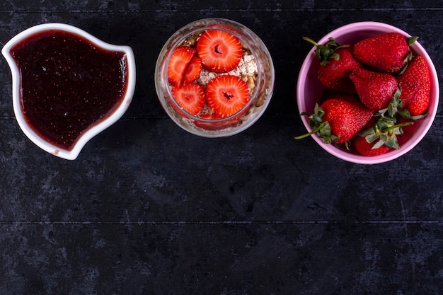 Foto gratuita vista dall'alto copia spazio granola con frutta e noci in un bicchiere con fragole in una ciotola rosa e marmellata