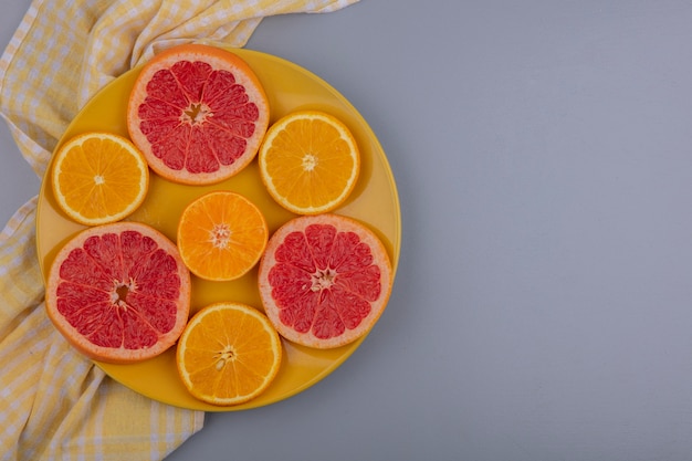 Top view  copy space grapefruit slices with orange slices on a yellow plate with a yellow checkered towel on a gray background