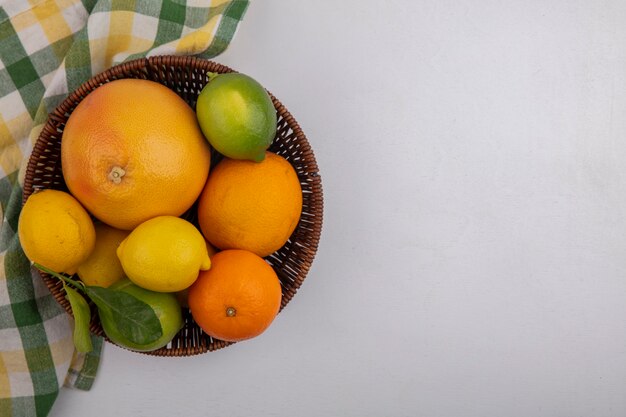 Top view  copy space grapefruit with oranges and lemons in a basket with a yellow green checkered towel on a white background