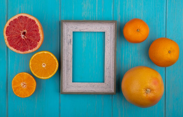 Top view  copy space gray frame with wedges and whole orange and grapefruit on turquoise background