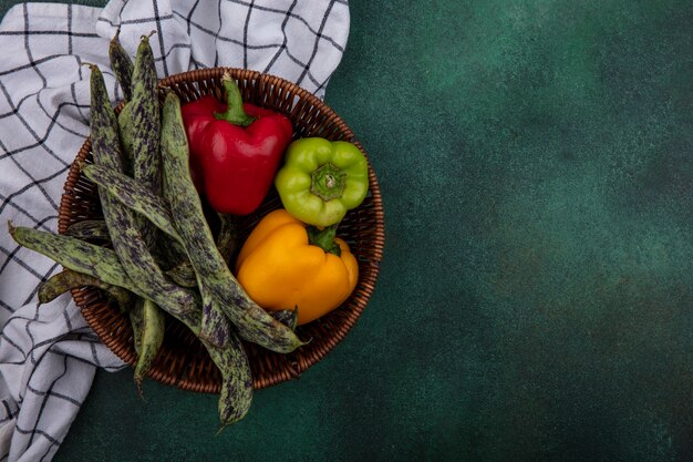 Top view  copy space green beans with bell peppers in a basket on a checkered towel  on a green background