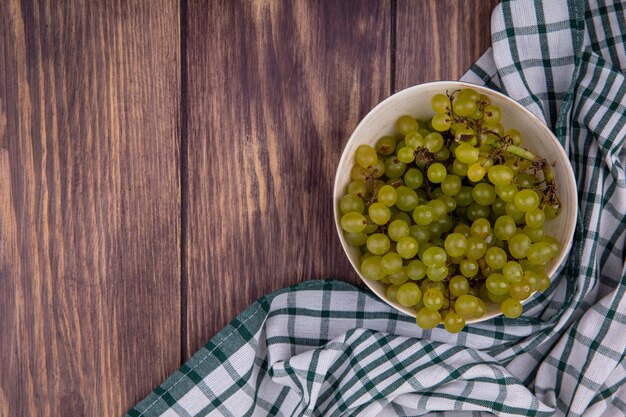 Top view copy space green grapes in bowl on green checkered towel on wooden wall