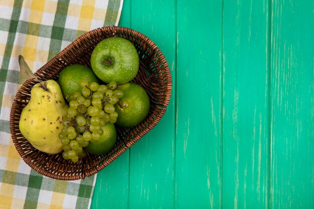 Вид сверху копией космического зеленого винограда с зеленым яблоком, мандаринами и грушей в корзине на зеленой стене