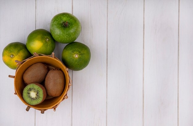 Вид сверху копией пространства киви в корзине с зелеными мандаринами и яблоком на белой стене