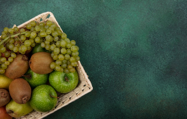 緑の背景にバスケットに青リンゴブドウと梨とトップビューコピースペースキウイ