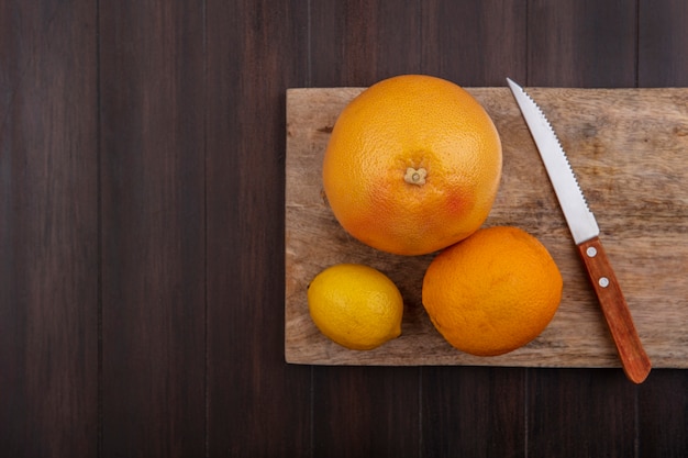 Вид сверху копией космического лимона с апельсином и грейпфрутом на разделочной доске с ножом на деревянном фоне