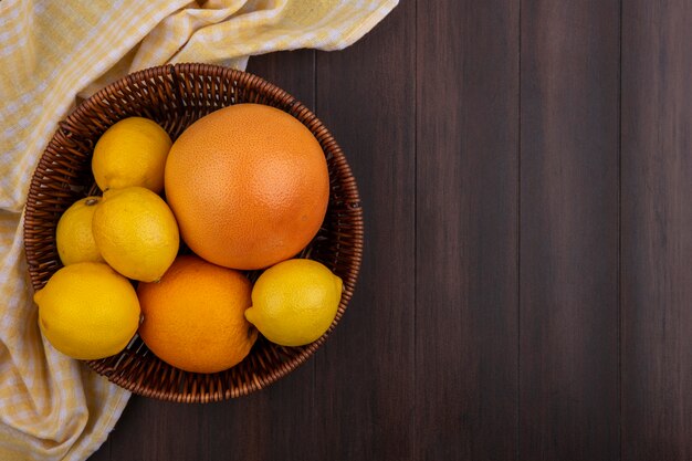 Top view  copy space lemons with orange and grapefruit in basket with yellow checkered towel on wooden background