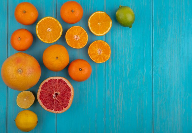 Вид сверху копией космического лайма с дольками и целым апельсином и грейпфрутом на бирюзовом фоне