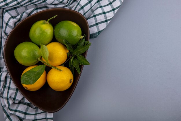 Top view  copy space limes with lemons in a bowl on a checkered towel  on a gray background