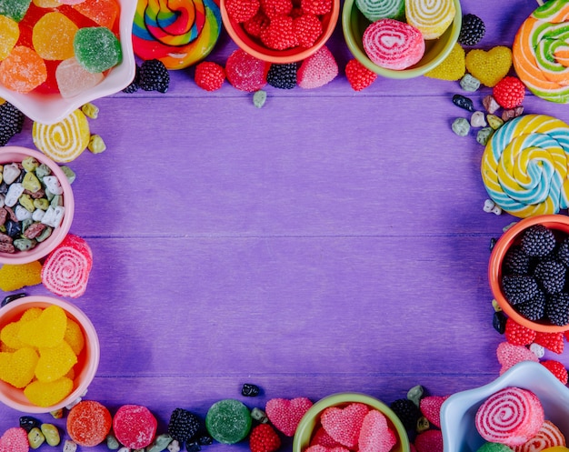 Top view copy space multi-colored marmalade with chocolate stones and colored icicles in saucers for jam on a purple background