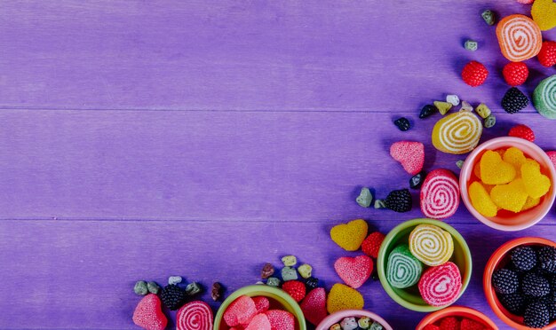 Top view copy space multi-colored marmalade with chocolate stones in saucers for jam on a purple background