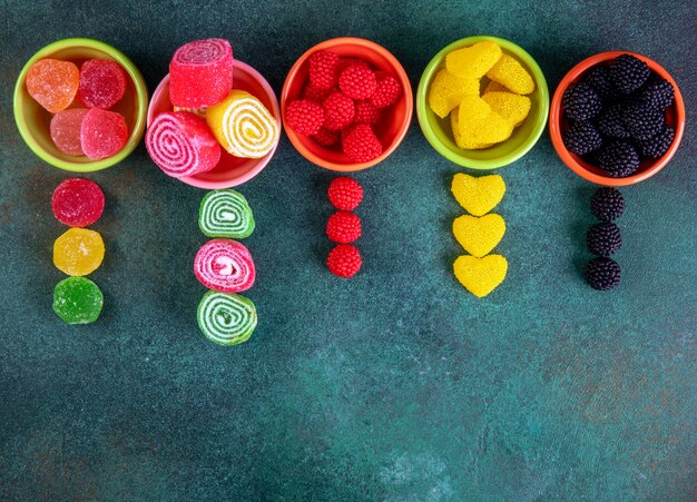 Top view copy space multi-colored marmalades in colored saucers for jam on a dark green background