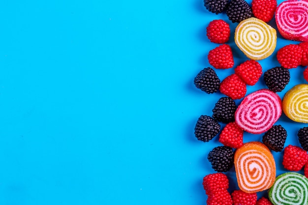 Top view copy space multi-colored marmalades with marmalades in the shape of raspberries and blackberries on a blue background