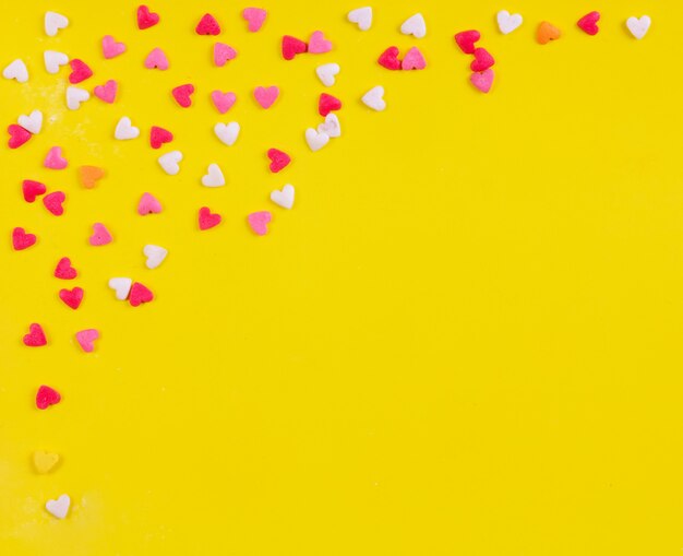 Top view copy space multi-colored sweets in the shape of a heart on a yellow background