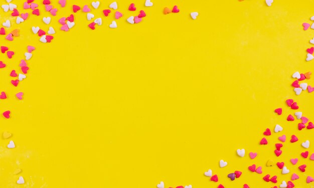 Top view copy space multi-colored sweets in the shape of a heart on a yellow background