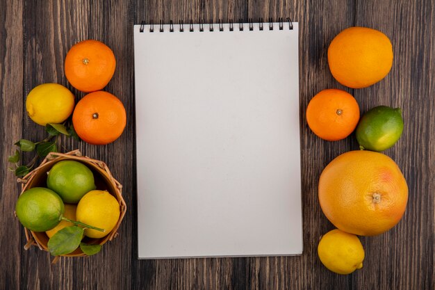 Top view  copy space notepad with grapefruit  oranges  lemons and limes in a basket on a wooden background