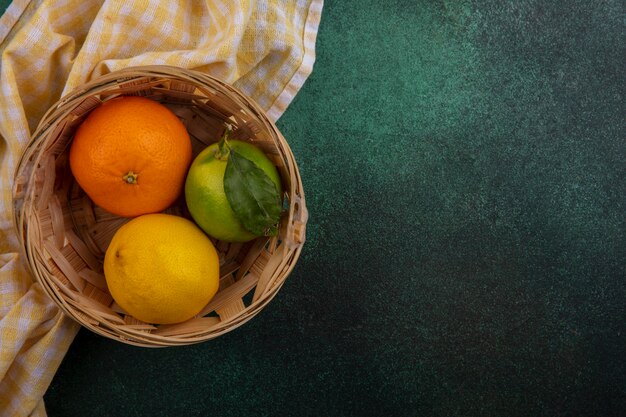 Top view  copy space orange with lemon and lime in basket with yellow checkered towel on green background
