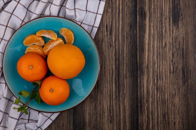 Top view  copy space oranges with peeled wedges on a blue plate on a checkered towel  on a wooden background