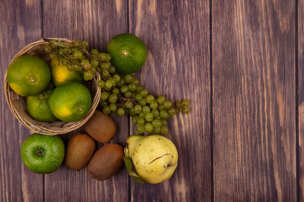 Top view copy space pear with kiwi tangerines apples and grapes in a basket on a wooden wall