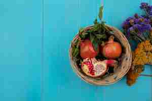 Free photo top view  copy space pomegranates in a basket with wildflowers on a turquoise background