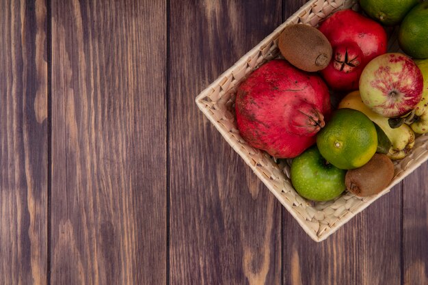 Вид сверху копией пространства гранатов с мандаринами, яблоками, грушами и киви в корзине на деревянной стене