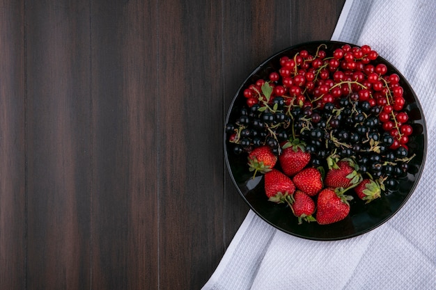 Top view copy space red and black currants with strawberries on a plate on a wooden background