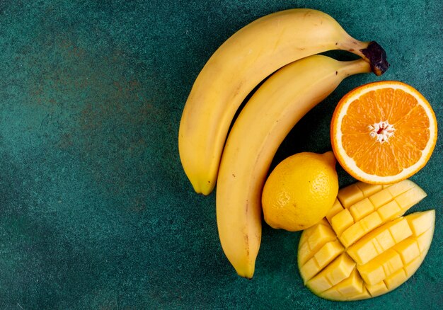 Top view copy space sliced mango with bananas half an orange and lemon on green