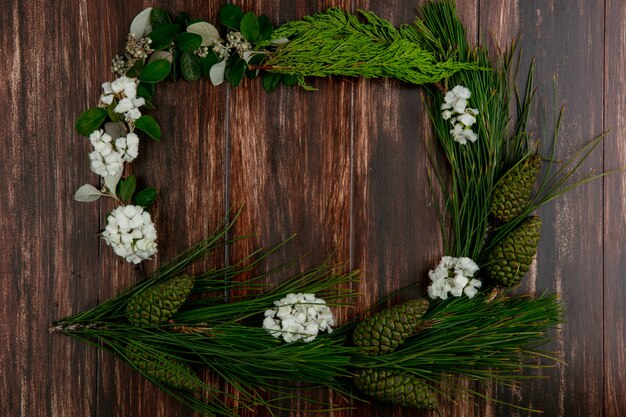 Top view copy space spruce branch with cones with white flowers around the edges on a wooden background