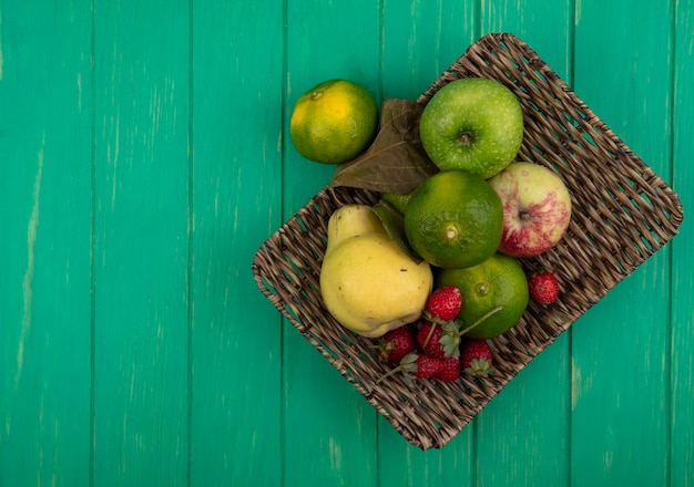 Mandarini dello spazio della copia di vista superiore con le mele della pera e la merce nel carrello delle fragole sulla parete verde