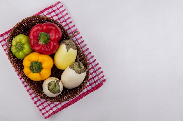 Top view  copy space white eggplant with colored bell peppers in a basket on a red checkered towel  on a white background