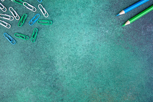 Top view copy space white green and blue paper clips with blue and light green pencils on a green background