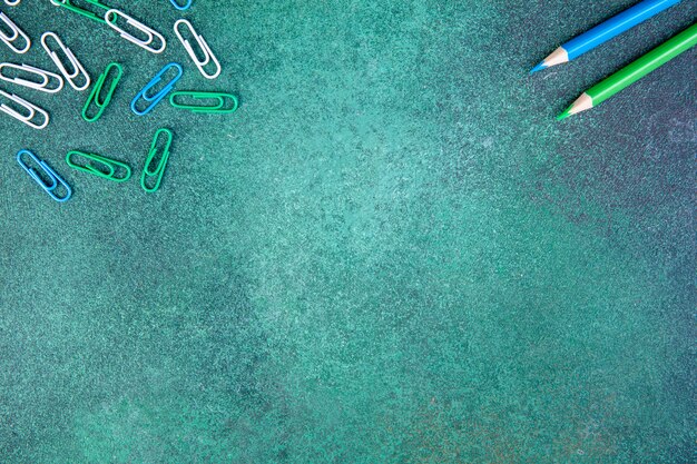 Top view copy space white green and blue paper clips with blue and light green pencils on a green background