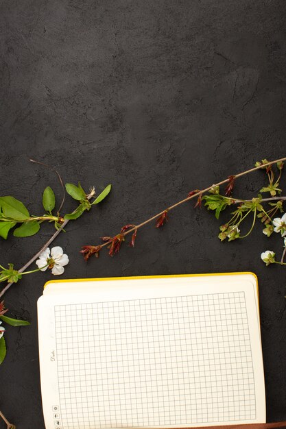 top view copybook along with flowers on the dark desk