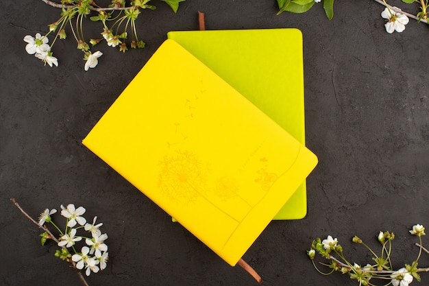 top view copybooks yellow and mustard colored around white flowers on the dark floor