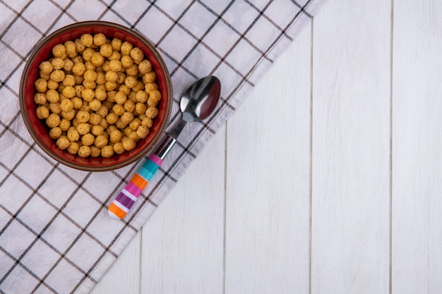 Top view of corn balls in a bowl with a colored spoon on a checkered towel on a white surface