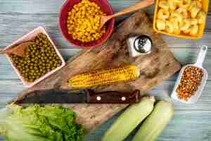 Foto gratuita vista superiore della pannocchia e del coltello di cereale sul tagliere con il sale della lattuga dei semi del cereale dei piselli su superficie di legno