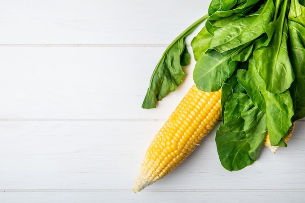 Top view of corn cob and spinach on wooden surface with copy space