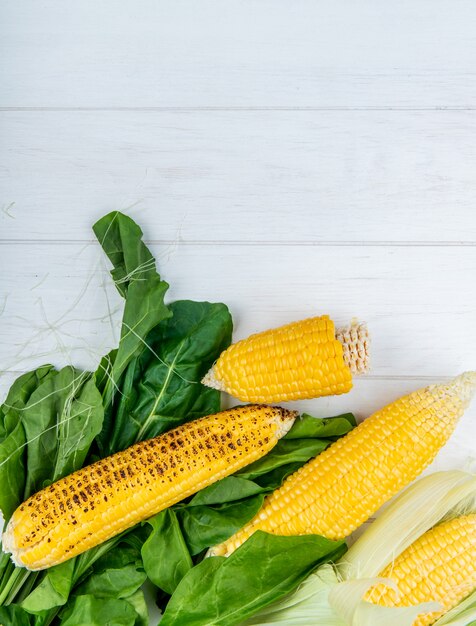 Top view of corn cobs and spinach on wood with copy space