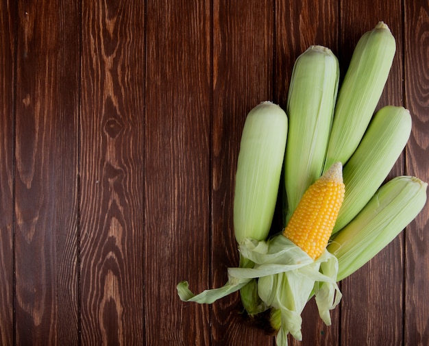 Free photo top view of corn cobs with shell on wood with copy space