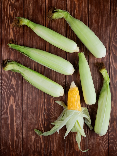 Free photo top view of corn cobs with shell on wooden surface 1