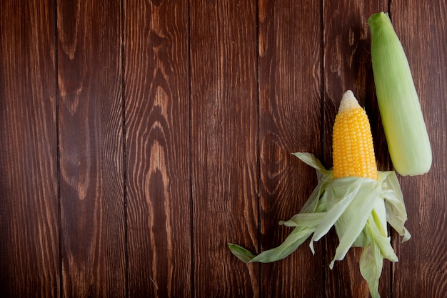 Free photo top view of corn cobs with shell on wooden surface with copy space