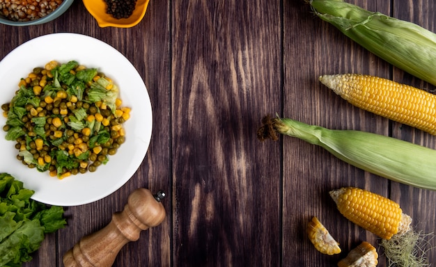 Foto gratuita vista superiore dell'insalata di mais con la lattuga tagliata e intera dei semi su superficie di legno