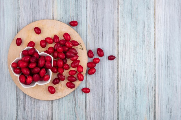 Top view of cornel berries in bowl and on cutting board and on wooden background with copy space